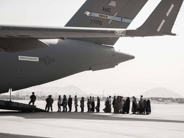Auf dem Flugfeld des Flughafens Kabul stehen Menschen vor einem Evakuierungsflugzeug Schlange.