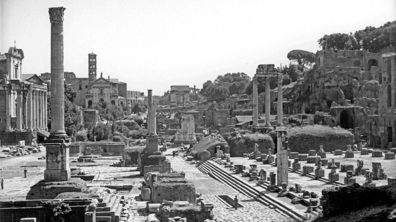 Ein Schwarz-Weiß-Foto von 1935 zeigt den Blick über das Forum Romanum nach Osten; im Vordergrund die Phokas- Säule; im Mittelgrund von links Tempel des Antoninus und der Faustina, Vesta-Tempel und Dioskuren-Tempel; im Hintergrund S. Francesca Romana und Titus-Bogen.