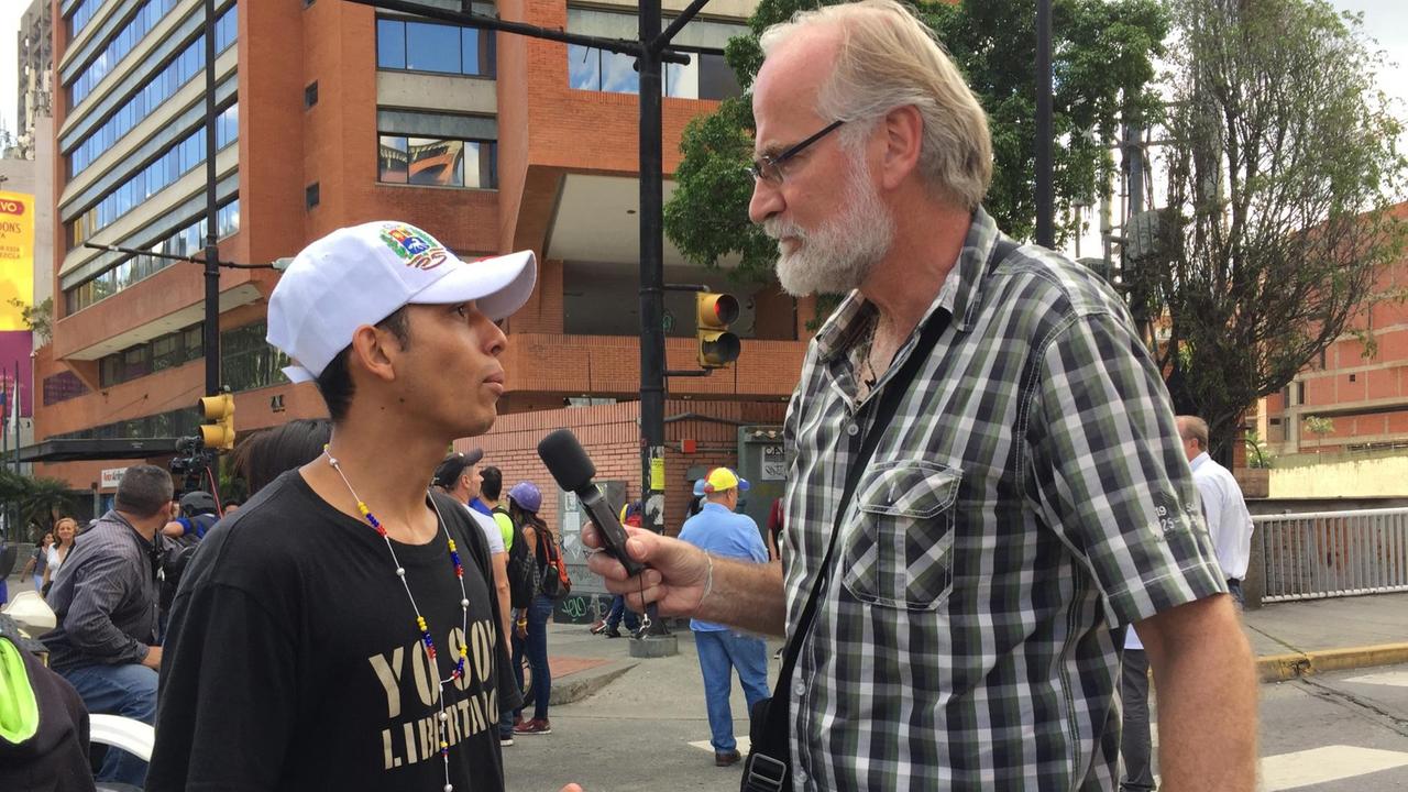 Burkhard Birke unterhält sich mit Mikrofon in der Hand mit einen Demonstranten in Caracas, Venezuela.