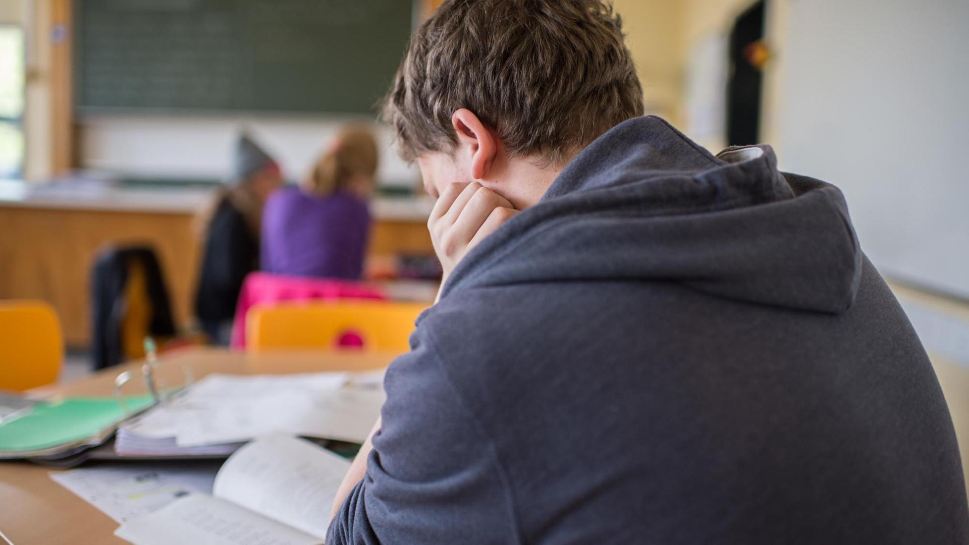 Ein Schüler sitzt im Unterricht an einem Schreibtisch und stützt seinen Kopf
