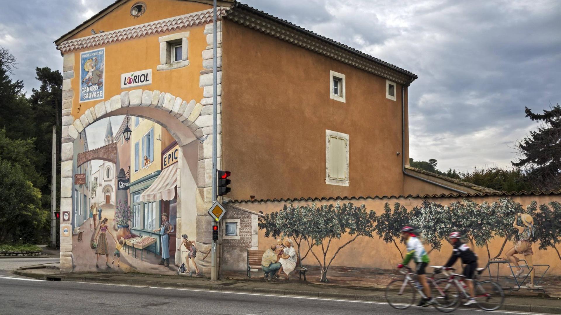Ein Gebäude mit einer alten gemalten Fassadenwerbung für den Nougat Canard Sauvage an der historischen Nationalstraße 7 bei Loriol-sur-Drome. Im Vordergrund 2 Sportler auf ihren Rennrädern.