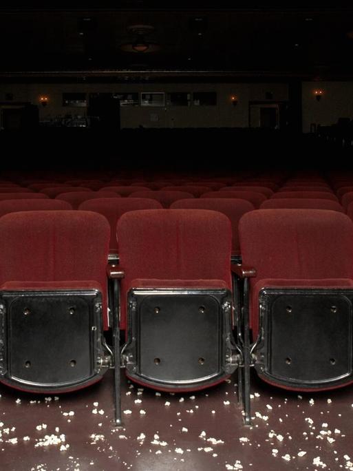 Ein leerer Kinosaal mit samtroten Sesseln, verstreutes Popcorn liegt vor der ersten Reihe auf dem Boden.