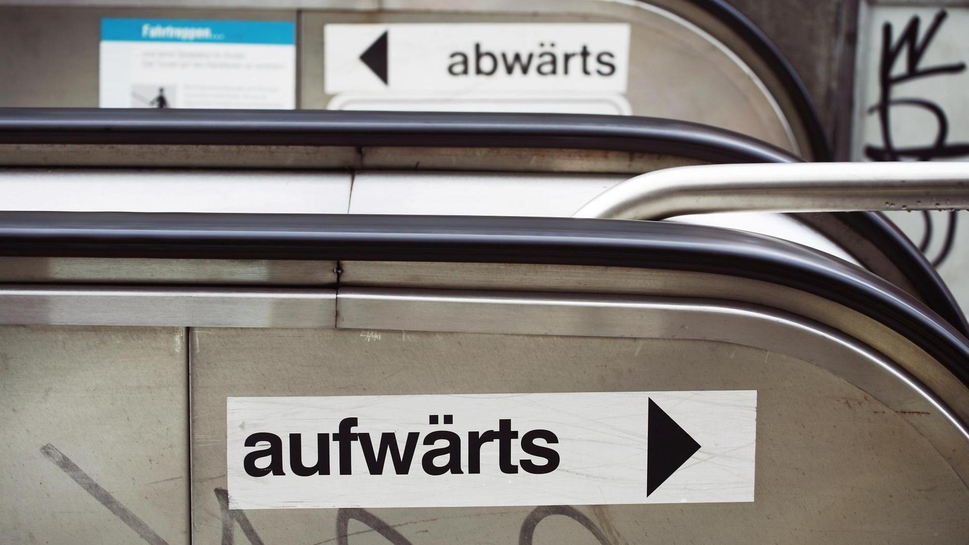 Zwei Schilder mit den Aufschriften "aufwärts" und "abwärts" kleben an einer Rolltreppe