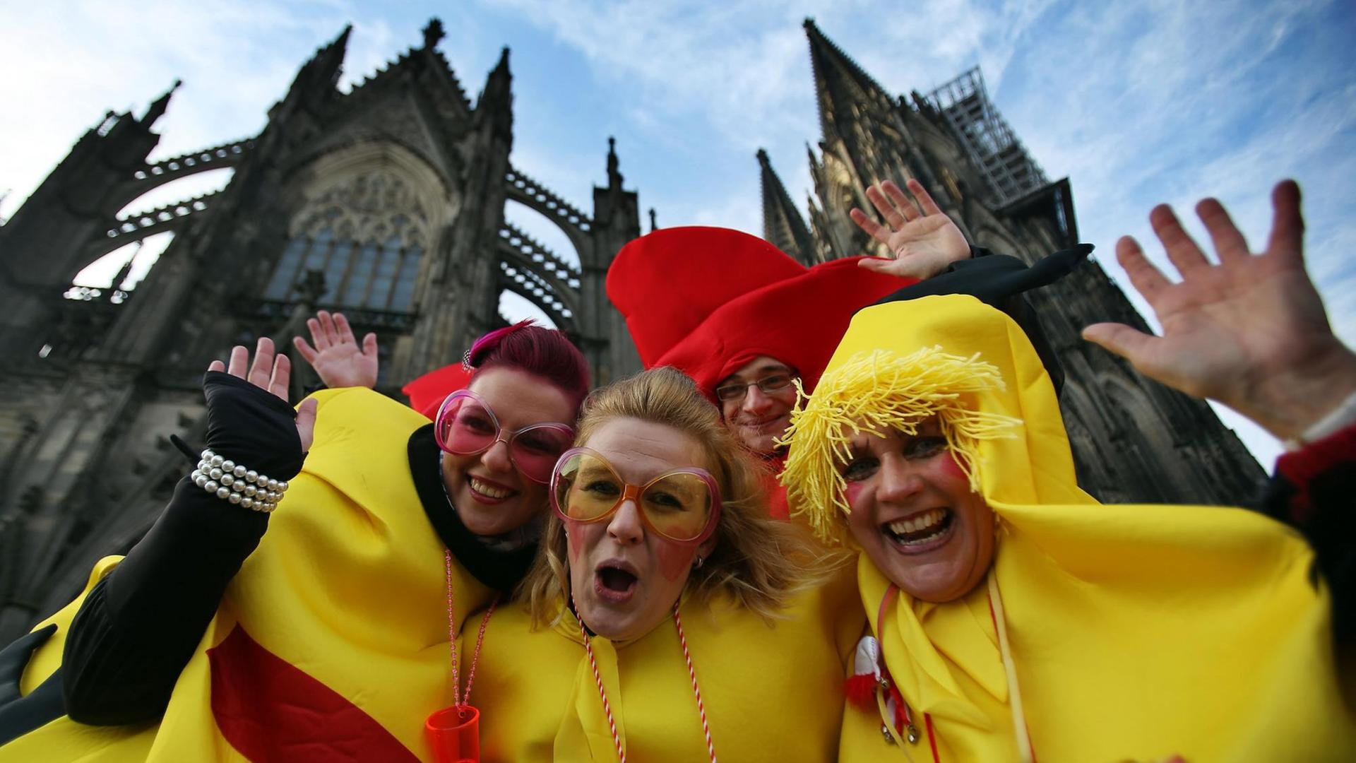 Vier Karnevalisten in Hühnerkostümen posieren vor dem Kölner Dom für die Kamera.