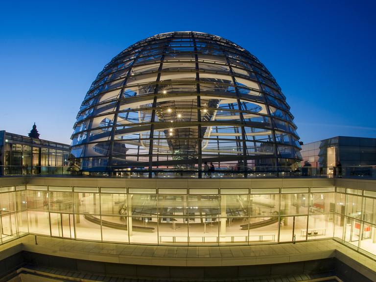 Im Abendlicht gehen in Berlin Besucher an der Kuppel des Reichstags entlang.