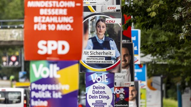 Viele bunte Wahl-Plakate von verschiedenen Parteien hängen neben einer Straße an Laternen.