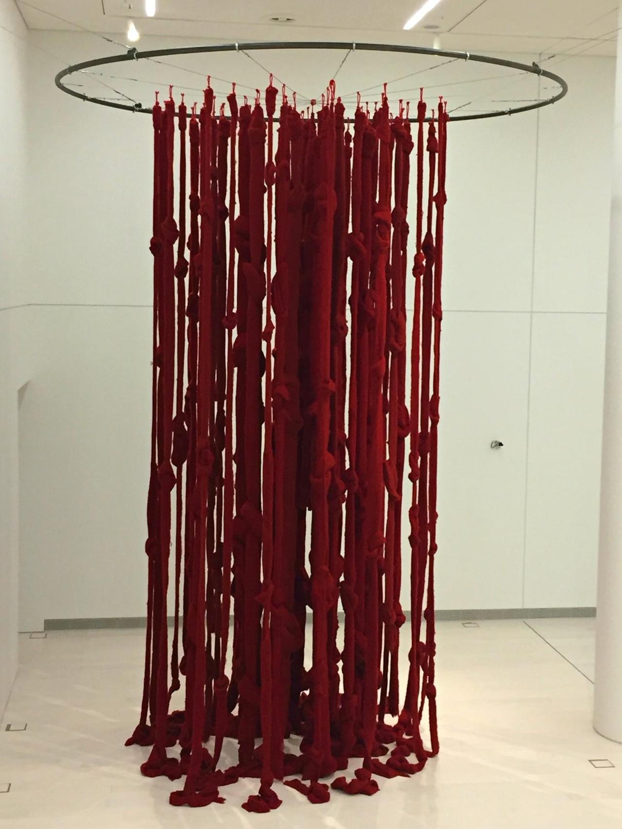 Dicke, verfilzte rote Wollfäden hängen von einem Rad, das an der Decke befestigt ist.