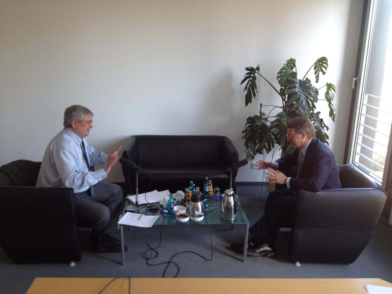 Eckhard Cordes (rechts) im Gespräch mit Klemens Kindermann, an einem niedrigen Tisch sich gegenüber sitzend, auf dem Tisch stehen Mikrofone, Kaffeekanne, Tassen und Flaschen.