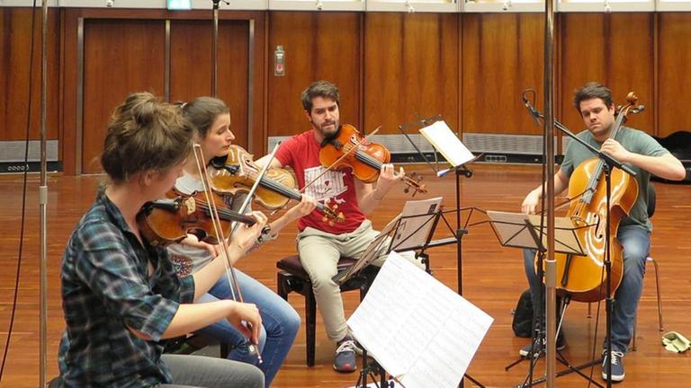 Die vier Musiker des Aris Quartett sitzen mit ihren Instrumenten im Kreis um ihre Notenpulte im Deutschlandfunk Kammermusiksaal.