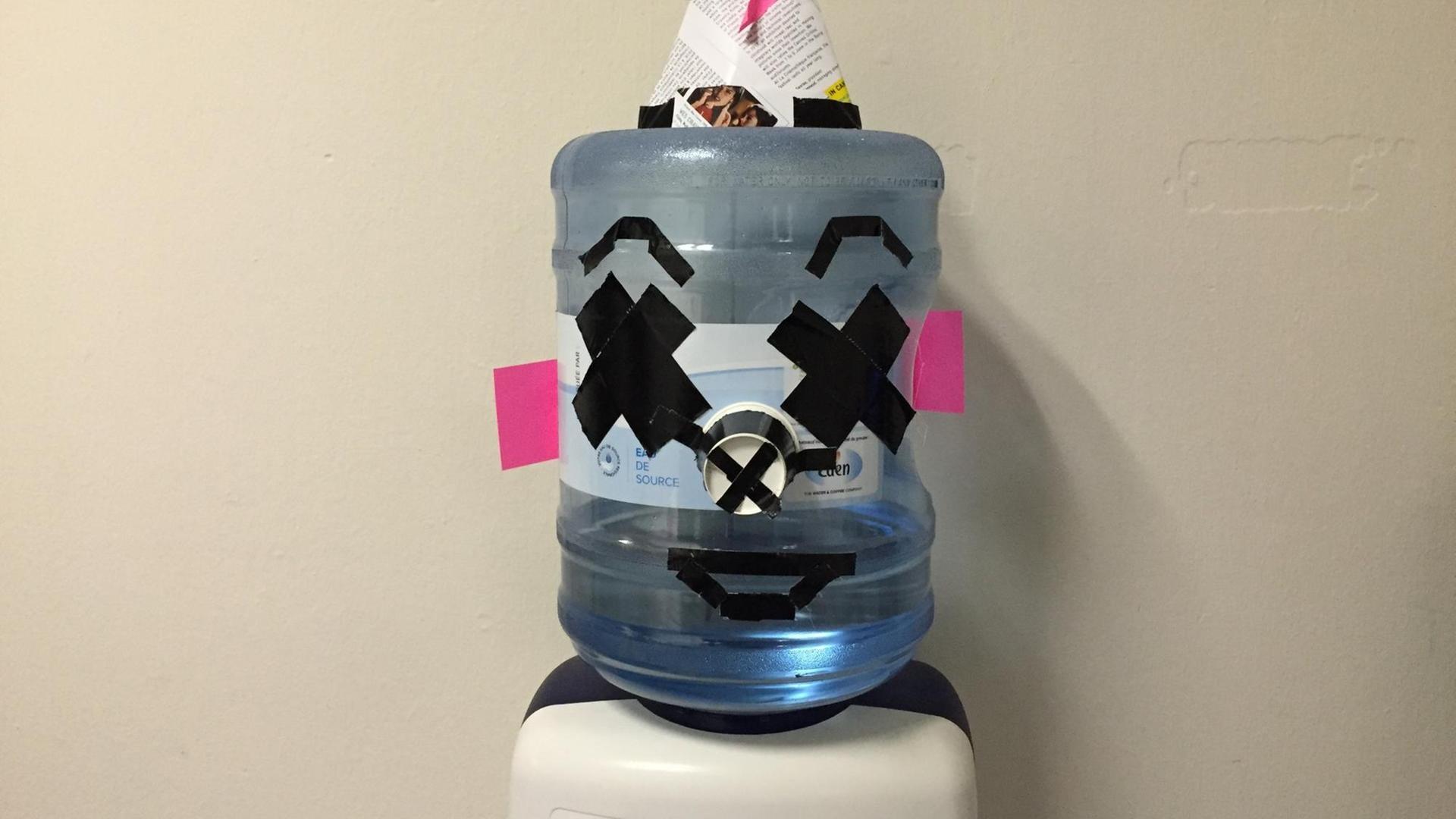 Bild von einem Wasserspender, der mit Klebestreifen und einem Papierhütchen aus Zeitung aussieht wie ein Kopf