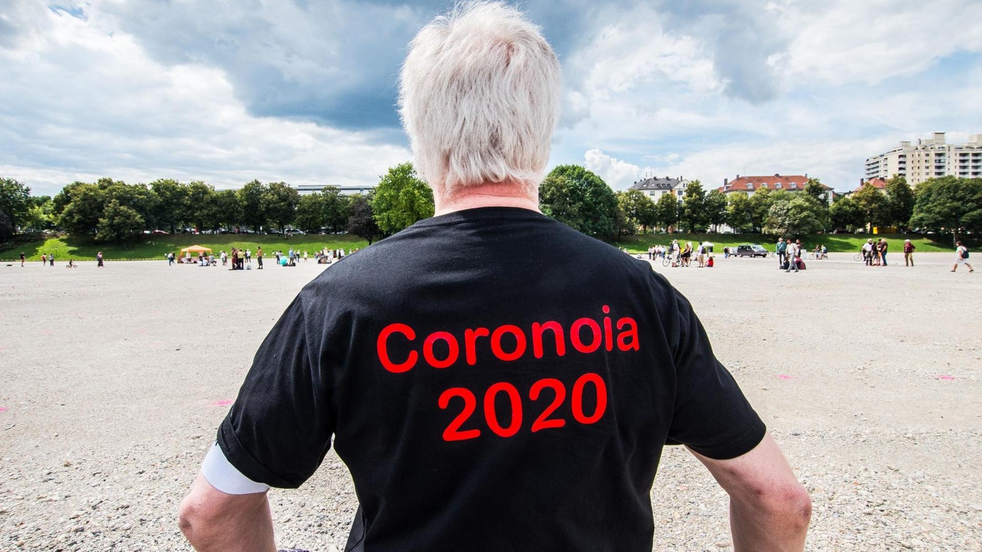 Man sieht einen Mann von hinten, der ein schwarzes T-Shirt mit dem roten Aufdruck "Coronoia 2020" trägt