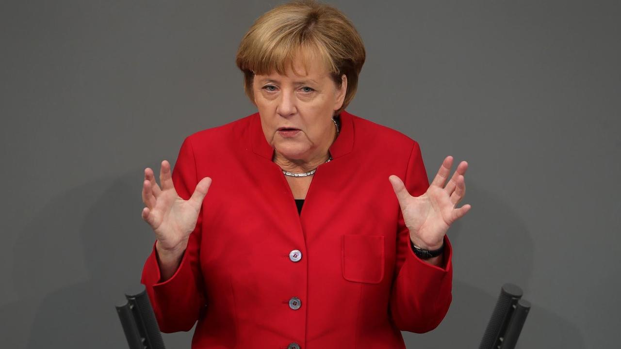 Merkel im roten Kostüm spricht und gestikuliert mit beiden Händen am Rednerpult.
