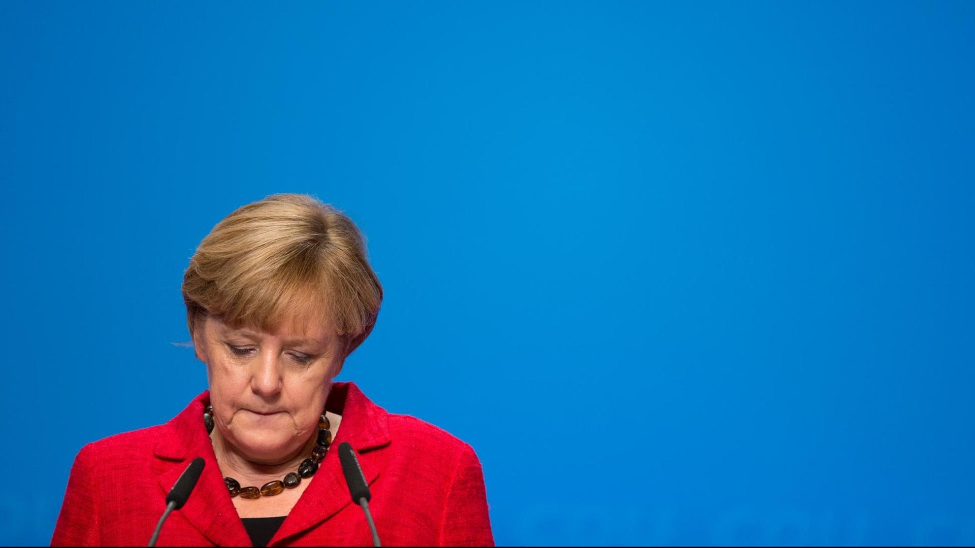 Bundeskanzlerin Angela Merkel vor einem Rednerpult; sie blickt nach unten.