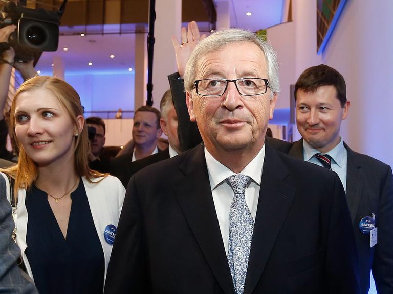 Jean-Claude Juncker am Abend der Europawahl in Brüssel. Hinter ihm stehen eine Frau und ein winkender Mann.