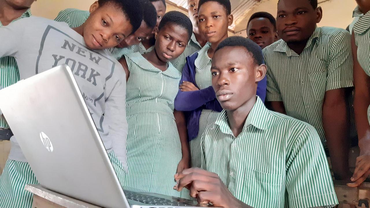 Schüler versammeln sich vor dem Laptop des Lehrers im ICT Unterricht.