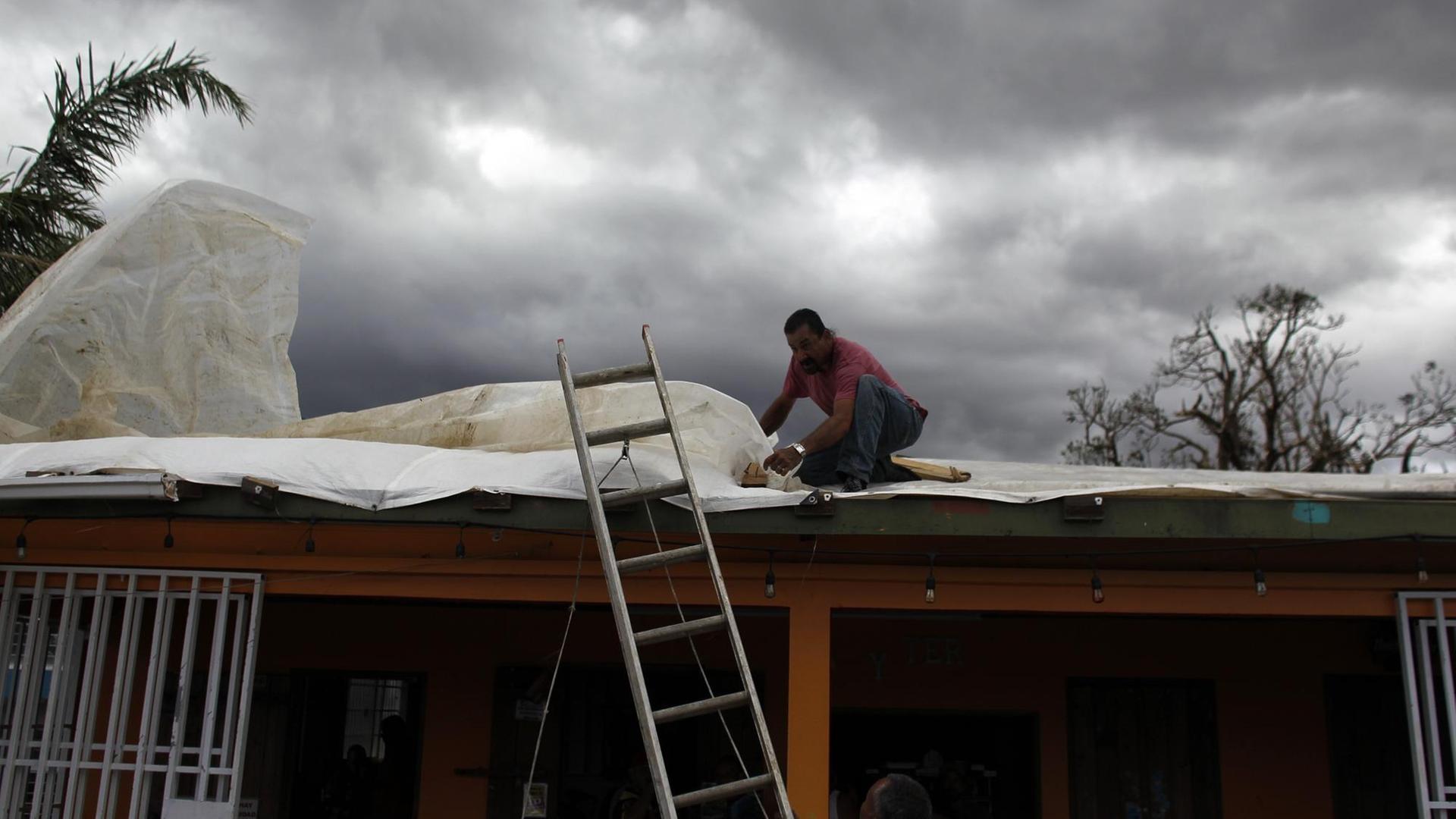 Ein Mann bringt eine Plane über einem beschädigten Dach eines Ladens in Aibonito/Puerto Rico an.