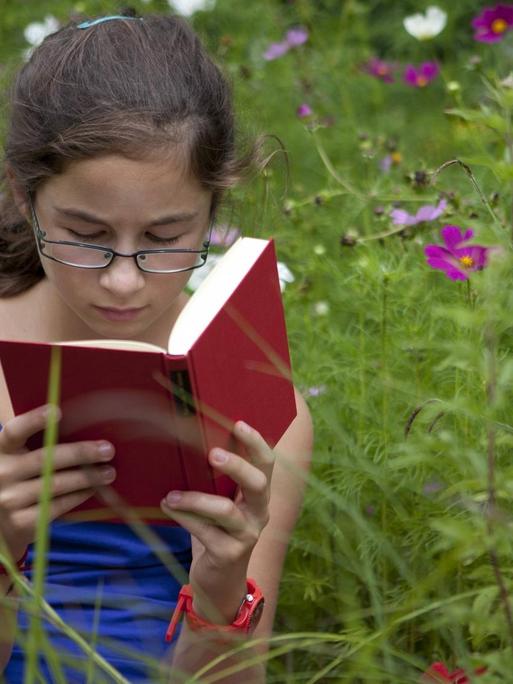 Ein elfjähriges Mädchen sitzt lesend auf einer Blumenwiese.