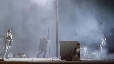 Auf der Bühne sieht man im Schneegestöber im Licht einer Art Straßenlaterne Georg Nigl als Peter, Elsa Dreisig in der Rolle der Natascha und das Ensemble.