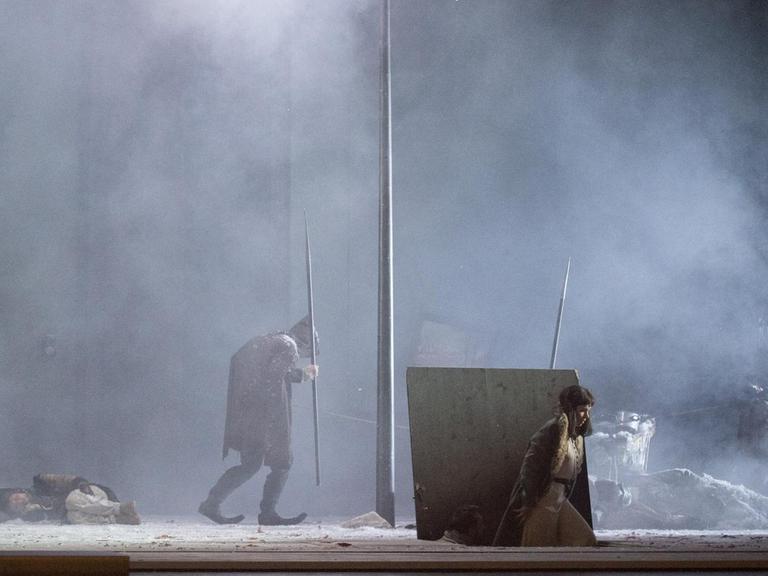 Auf der Bühne sieht man im Schneegestöber im Licht einer Art Straßenlaterne Georg Nigl als Peter, Elsa Dreisig in der Rolle der Natascha und das Ensemble.