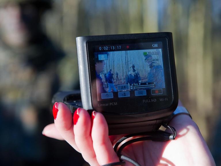 Eine weibliche Hand hält eine Kamera, mit der Soldaten gefilmt werden
