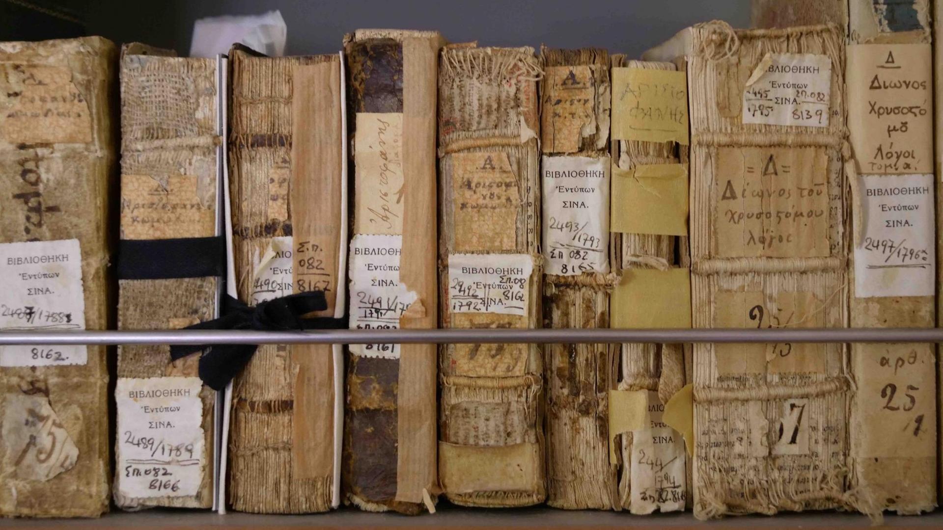 In einem Regal stehen sehr alte Bücher nebeneinander, die Buchrücken in Auflösung begriffen.