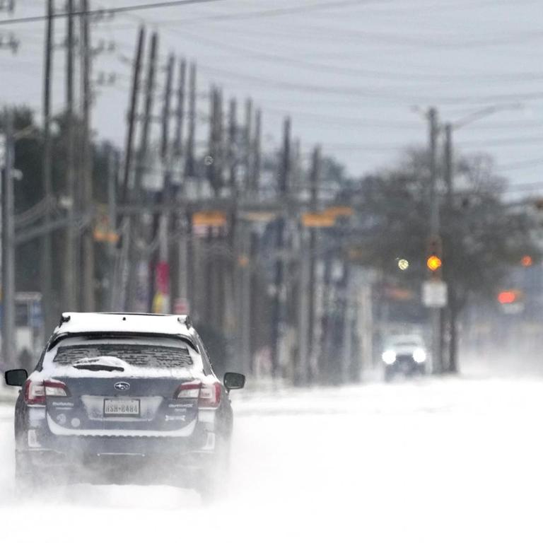 Ein Auto fährt auf einer zugeschneiten Straße. Im südlichen US-Bundesstaat Texas sind wegen ungewöhnlich kalten Winterwetters Hunderttausende Menschen mindestens zeitweise ohne Strom gewesen.