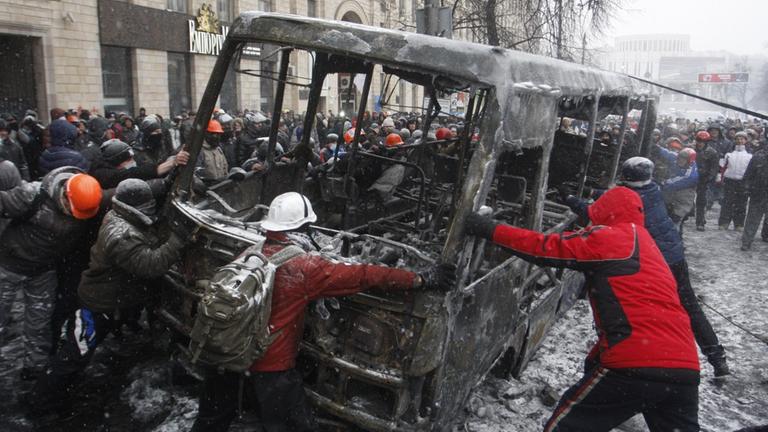 ITAR-TASS: KIEV, UKRAINE. JANUARY 21, 2014. Protesters overturn a burnt out vehicle at the site of a stand off between riot police and demonstrators in Grushevsky Street. On 16 January 2014 Ukraine's parliament, Verkhovna Rada, adopted tougher security la