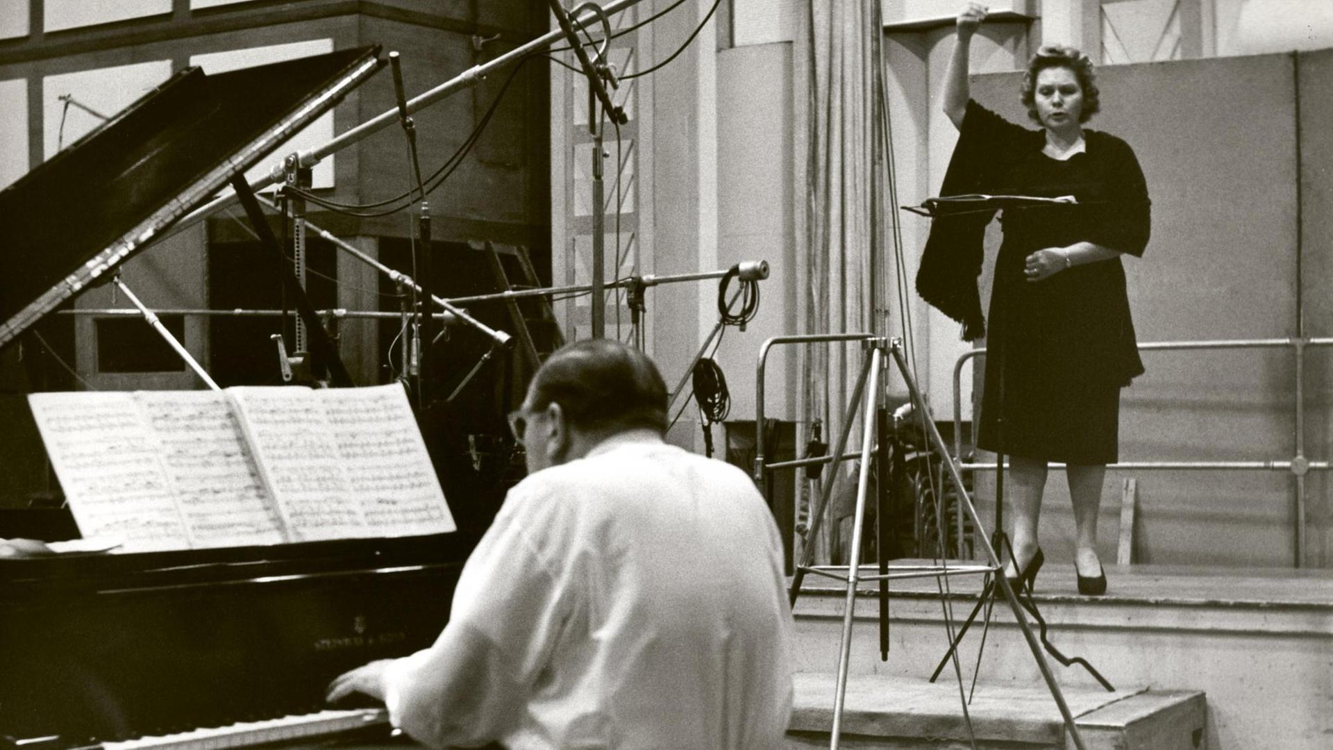 Links vorne ein Flügel, daran ein Pianist mit Rücken zum Betrachter. Rechts hinten eine Sängerin vor einem Mikrofon.