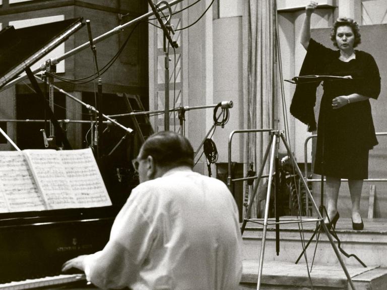 Links vorne ein Flügel, daran ein Pianist mit Rücken zum Betrachter. Rechts hinten eine Sängerin vor einem Mikrofon.