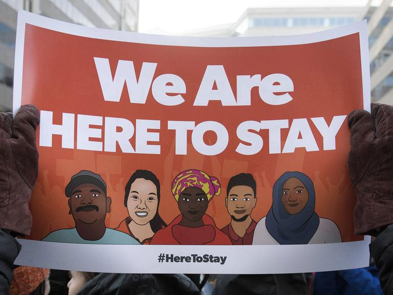 Ein Demonstrant hält ein Plakat mit dem Spruch "We are here to stay" hoch.