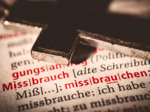 Christliches Kreuz auf einem Buch mit Stichwort MISSBRAUCH liegend