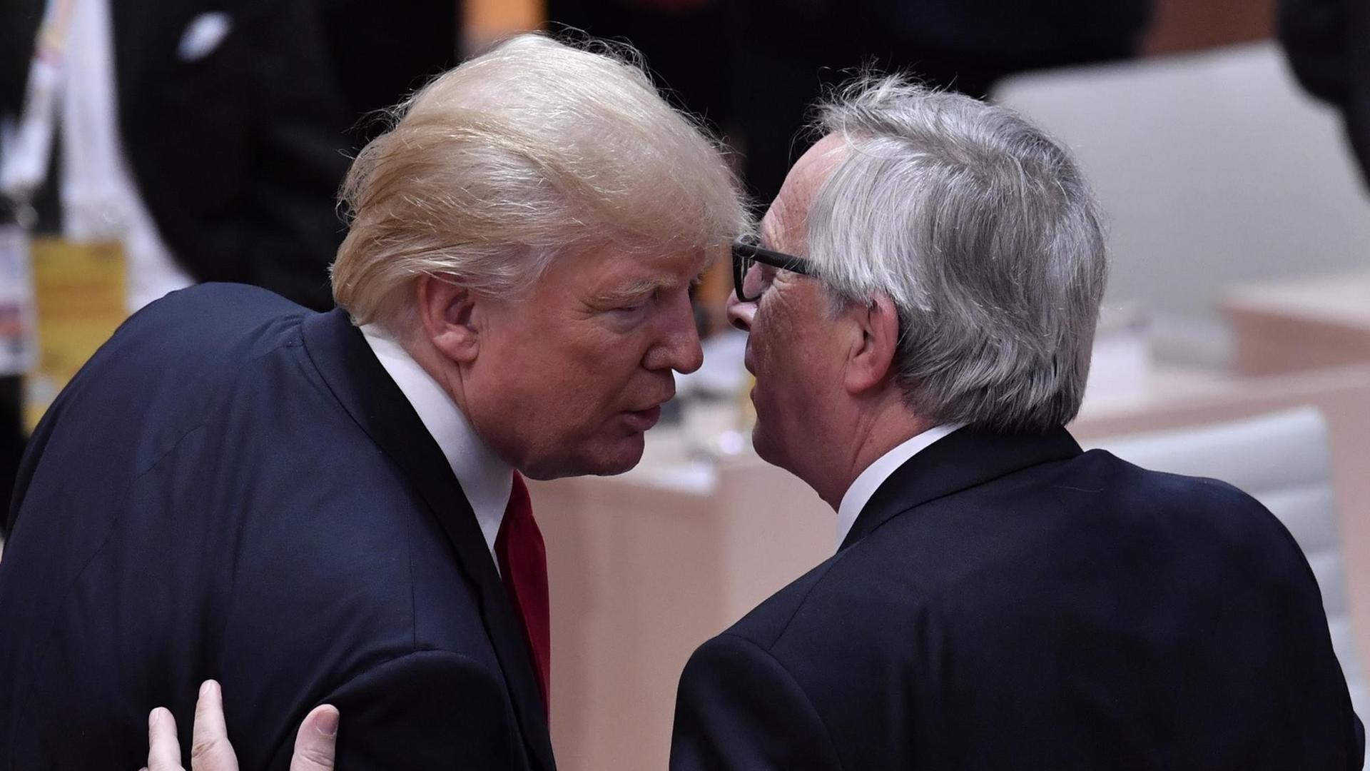 Zu sehen sind EU-Kommissionspräsident Jean-Claude Juncker (r.) und US-Präsident Donald Trump während des G20-Gipfels in Hamburg am 8. Juli 2017. Sie sind von hinten fotografiert und unterhalten sich einander eng zugewandt.