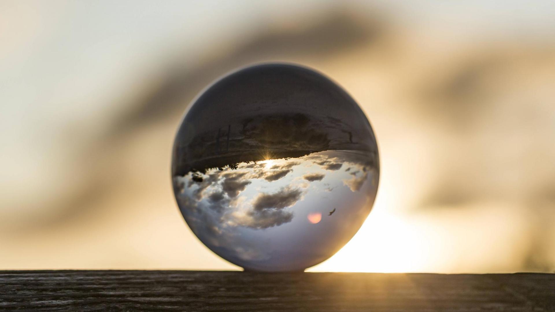 Eine Glaskugel, in der sich der Himmel und Wolken seitenverkehrt spiegeln.