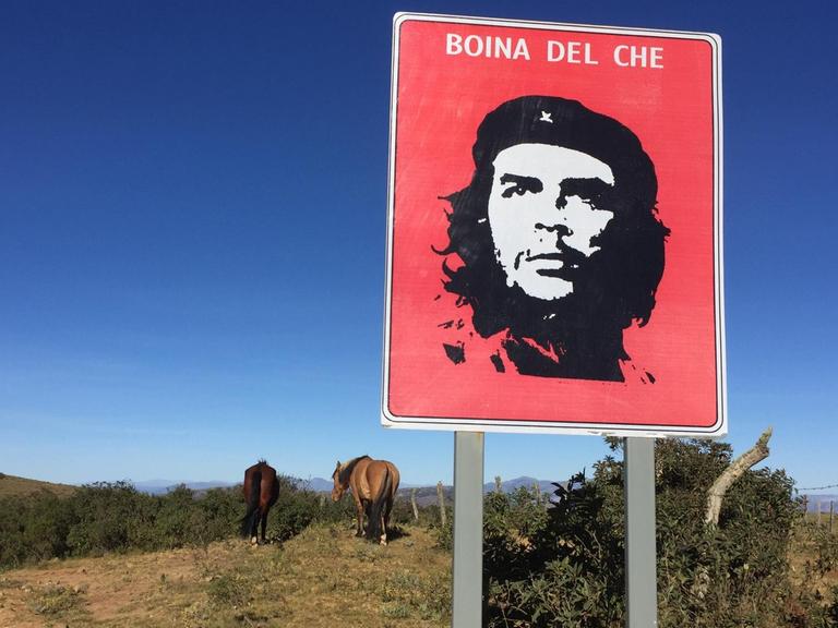 Ein Schild mit Che Guevara im bolivianischen Hinterland neben Pferden.