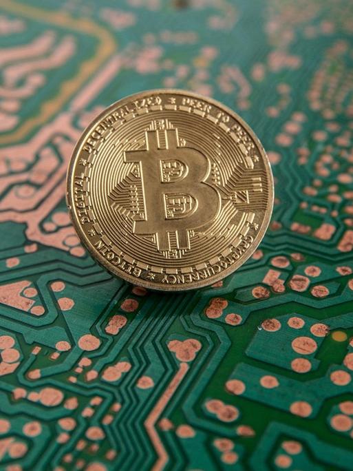 Auf dem Bild ist eine Münze mit einem "B" drauf zu sehen. Sie steht vor dem Hintergrund eines Computerchips.