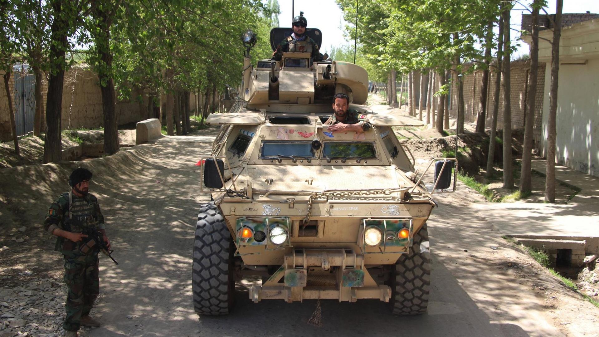 Zwei Männer schauen aus einem Panzer, der auf einer Straße steht. Daneben steht ein weiterer, bewaffneter Mann.
