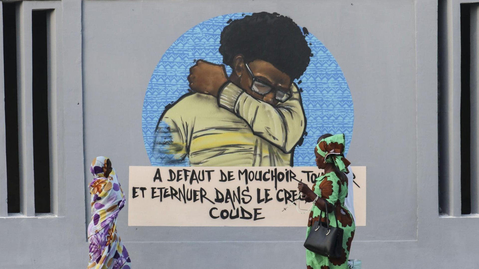 In Dakar (Senegal) gehen Menschen an einer Wandmalerei vorbei, die auf Hygienemaßnahme bezüglich Corona verweist.