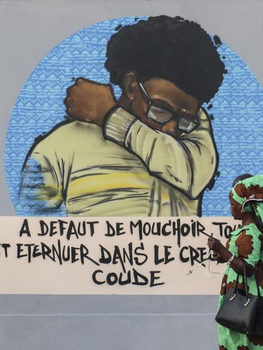 In Dakar (Senegal) gehen Menschen an einer Wandmalerei vorbei, die auf Hygienemaßnahme bezüglich Corona verweist.