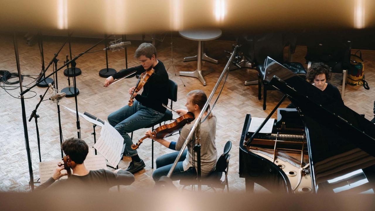 Die Mitglieder des Klavierquartetts sind von einer Galerie aus fotografiert worden, während sie in einem Saal mit Holzparkett musizieren.