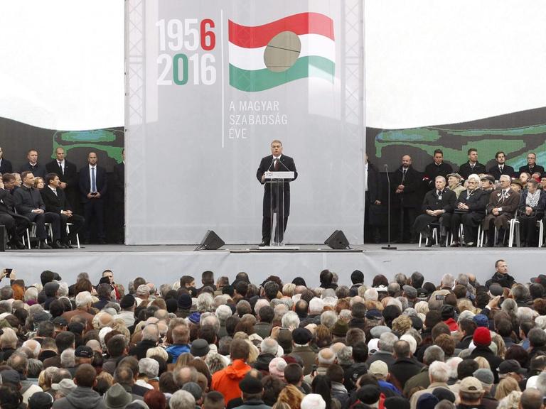 Der ungarische Ministerpräsident Orban steht auf einem Podium vor dem Parlament in Budapest und hält eine Rede anlässlich des Volksaufstandes von 1956.
