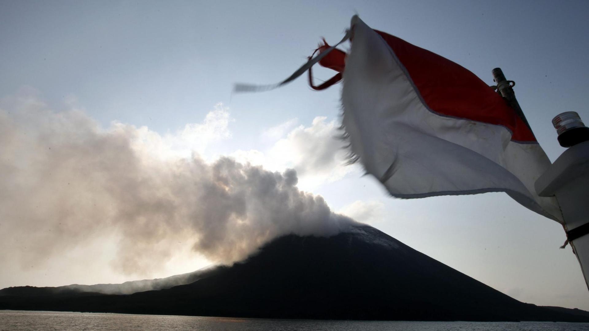 Blick auf den Anak Krakatau vom Meer aus. Im Vordergrund weht eine indonesische Flagge.