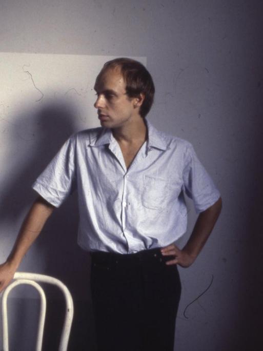 Brian Eno posiert auf einem Farbfoto aus den 70er Jahren mit Zigarette und Stuhllehne.
