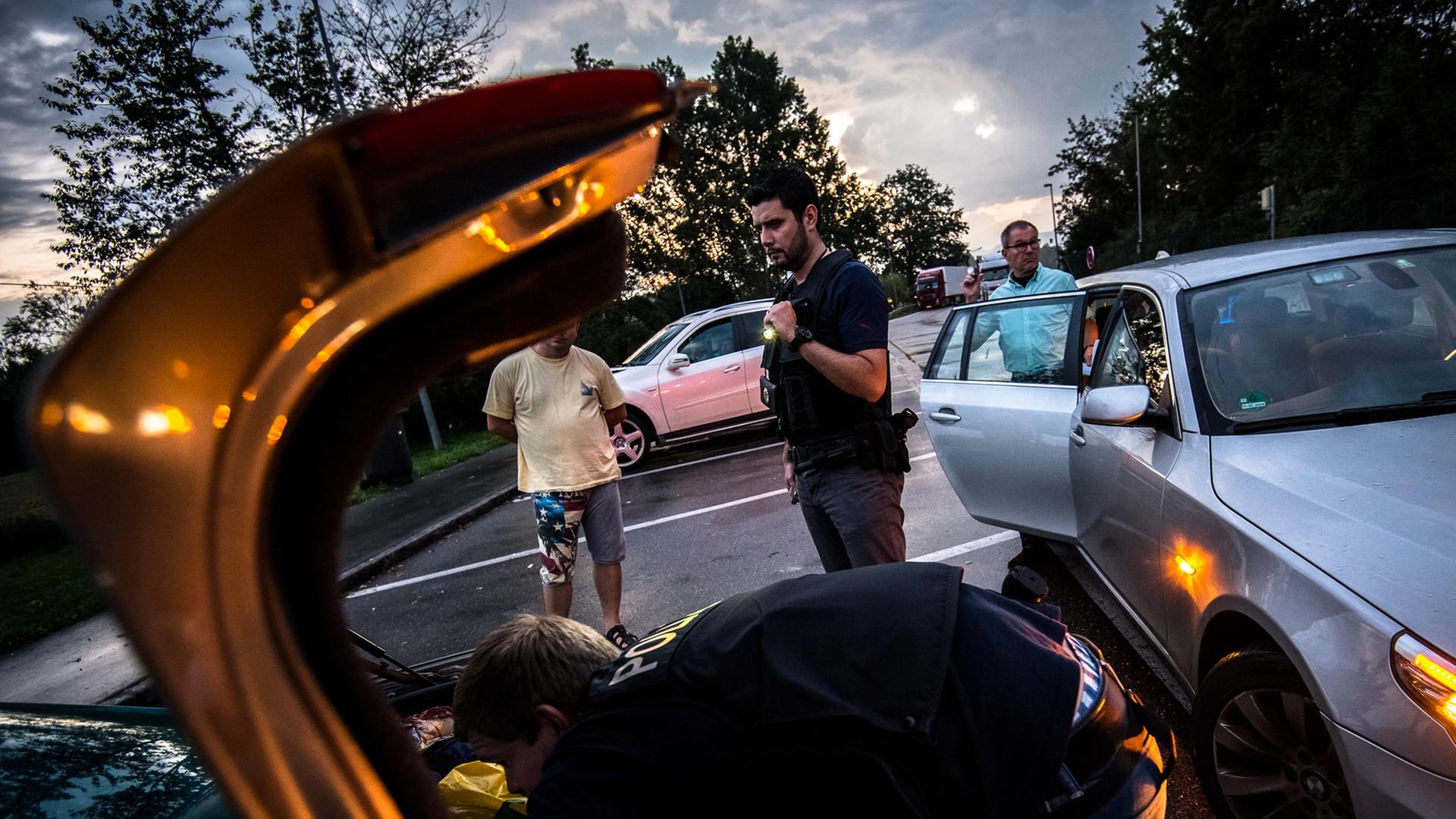 Ein Bundespolizist durchsucht den Kofferraum eines Autos, im Hintergrund stehen mehrere Männer.