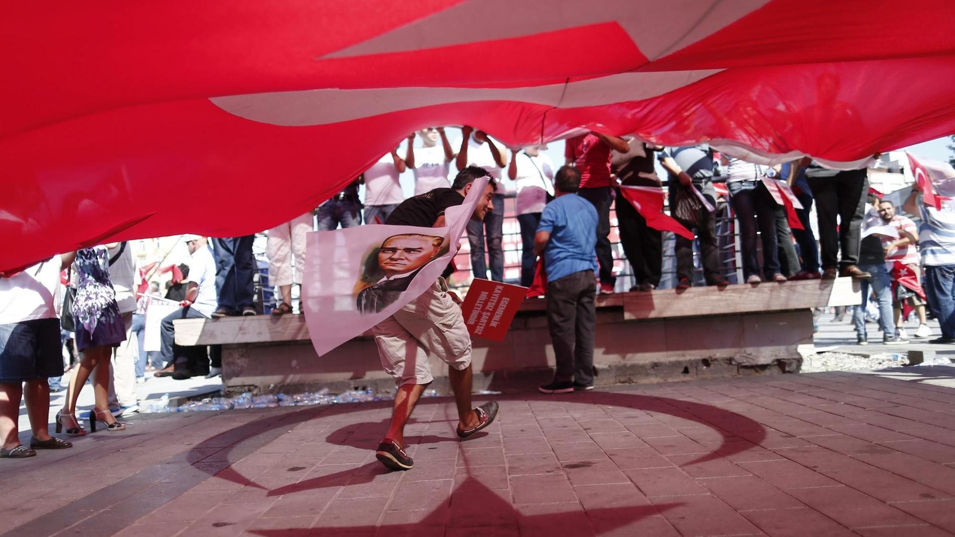 Ein Demonstrant steht unter einer türkischen Flagge und hält eine Fahne mit dem Konterfei von Staatsgründer Atatürk in der Hand.