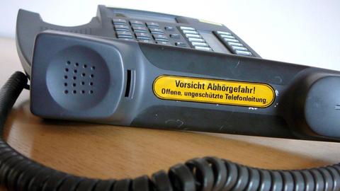 Ein Telefon mit dem Aufdruck "Vorsicht Abhörgefahr" liegt auf einem Schreibtisch.