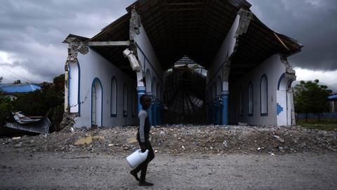 Ein haitianischer Junge läuft mit einer Plastikflasche in der Hand an den Ruinen einer zerstörten Kirche vorbei.