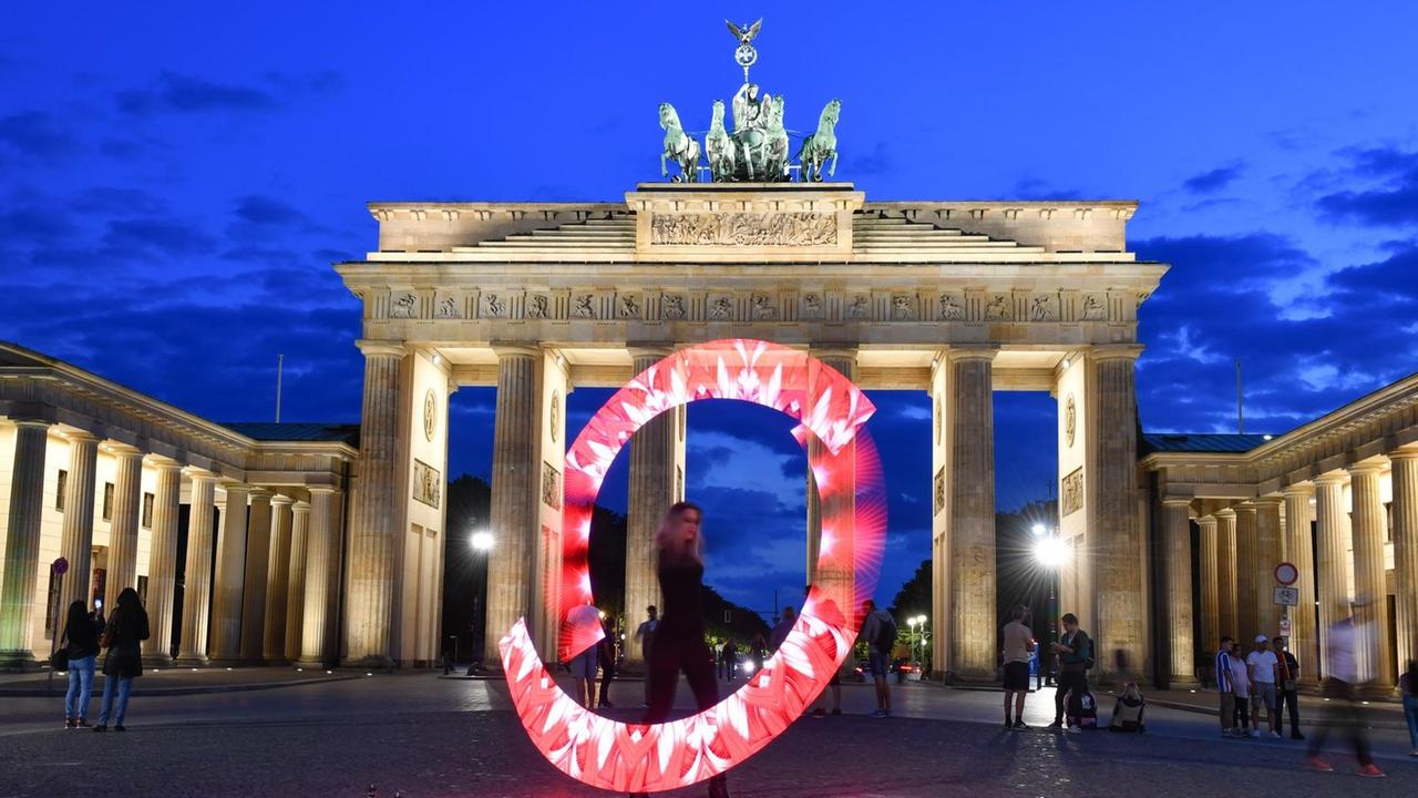 Eine Lichtkünstlerin performt mit roten Lichtern vor dem Brandenburger Tor. Mit leuchtenden Mahnmalen hat die Veranstaltungsbranche am Abend auf ihre Lage in der Corona-Krise hingewiesen.