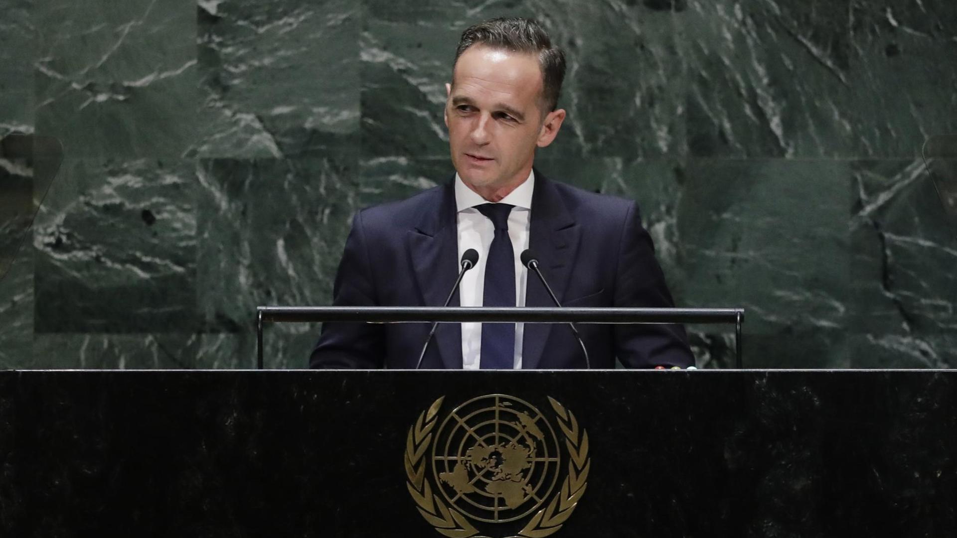 Maas steht mit leichtem Lächeln am Rednerpult vor der Marmorwand des UNO-Präsidiums und spricht in zwei Mikrofone. Er trägt einen dunkelblauen Anzug.