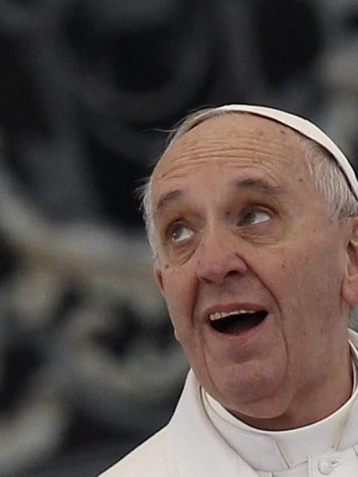 Der Papst blickt lächelnd nach oben. Im Hintergrund sieht man unscharf die Fassade eines historischen Gebäudes.