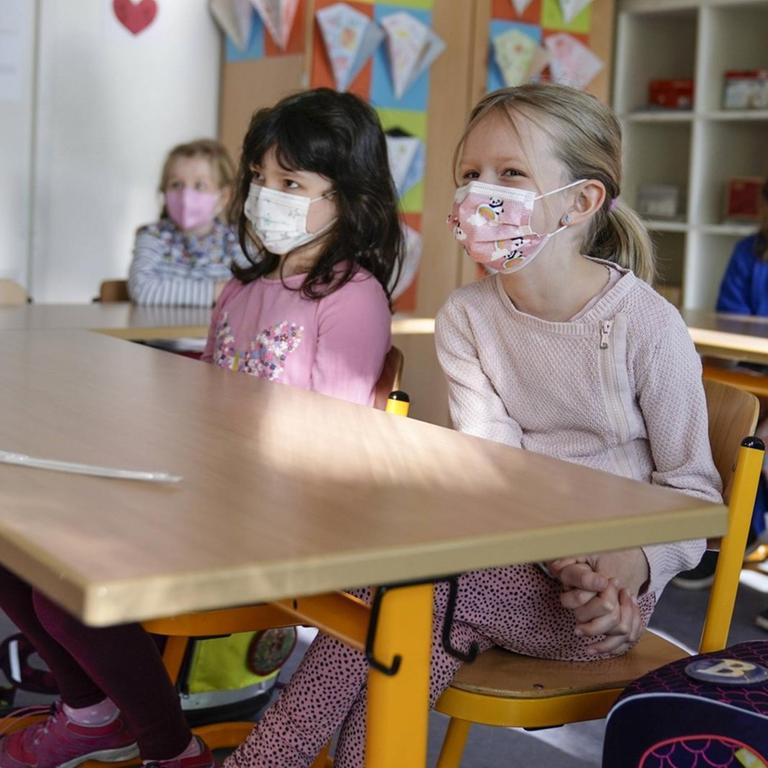 Grundschülerinnen sitzen mit Mund-Nasen-Schutz in einem Klassenraum in Düsseldorf, vor ihnen liegen die Corona-Teststäbchen für den sogenannten Lolli-Test 
